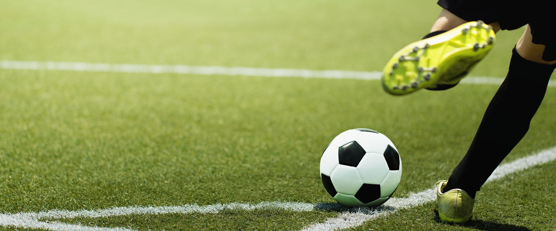 Foot of a child football player and ball on the football field, kicking a corner kick