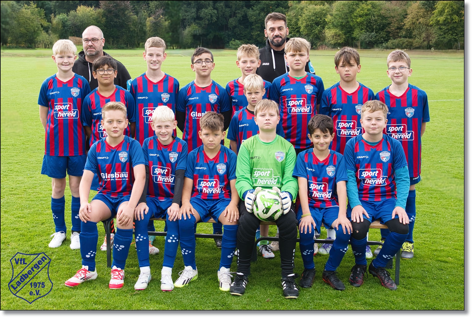 Eine Jugend-Fußballmannschaft posiert lächelnd in blau-roten Trikots auf dem Feld