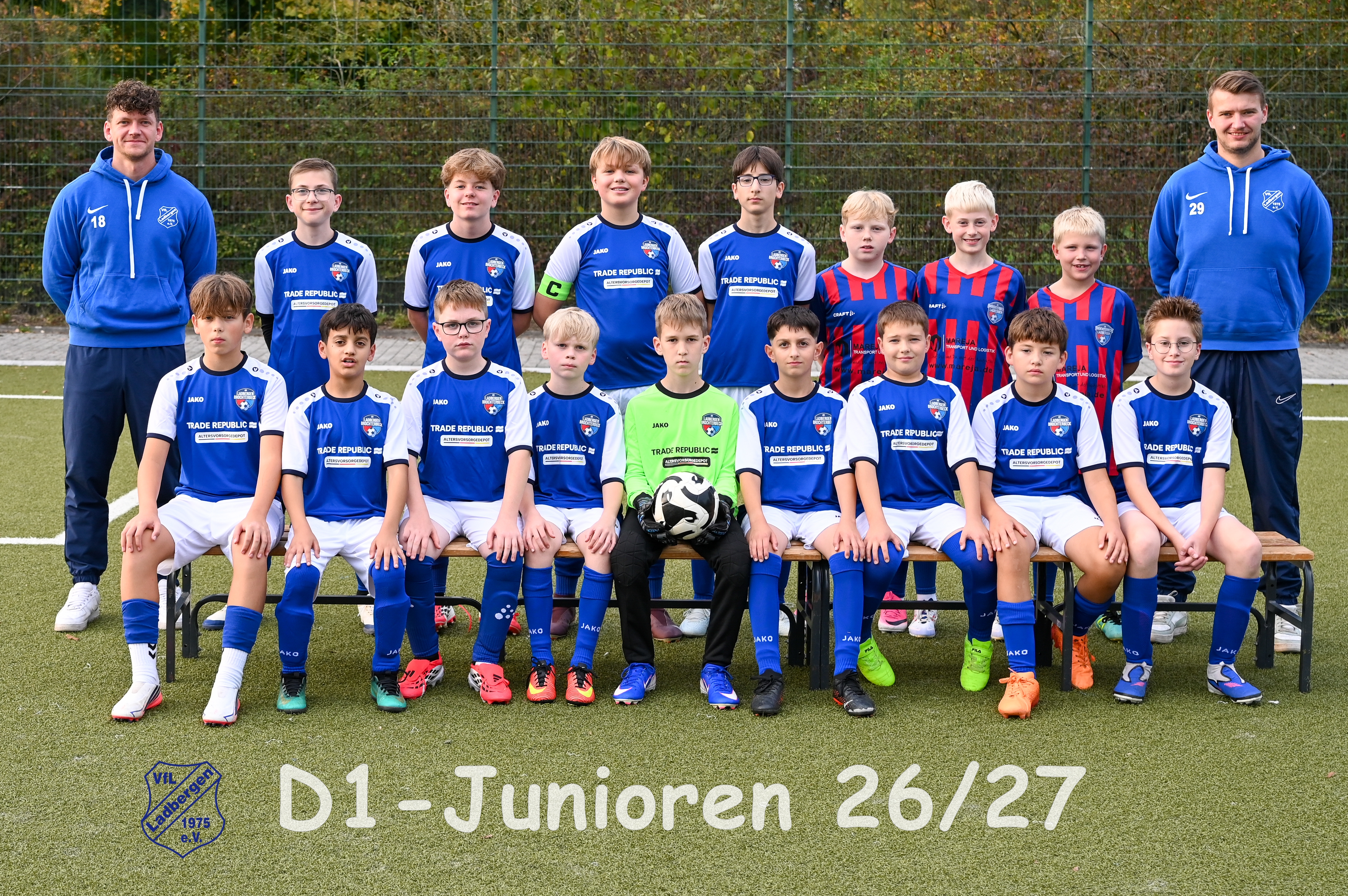Laechelndes Jugendfussballteam in blauen Trikots mit zwei Trainern