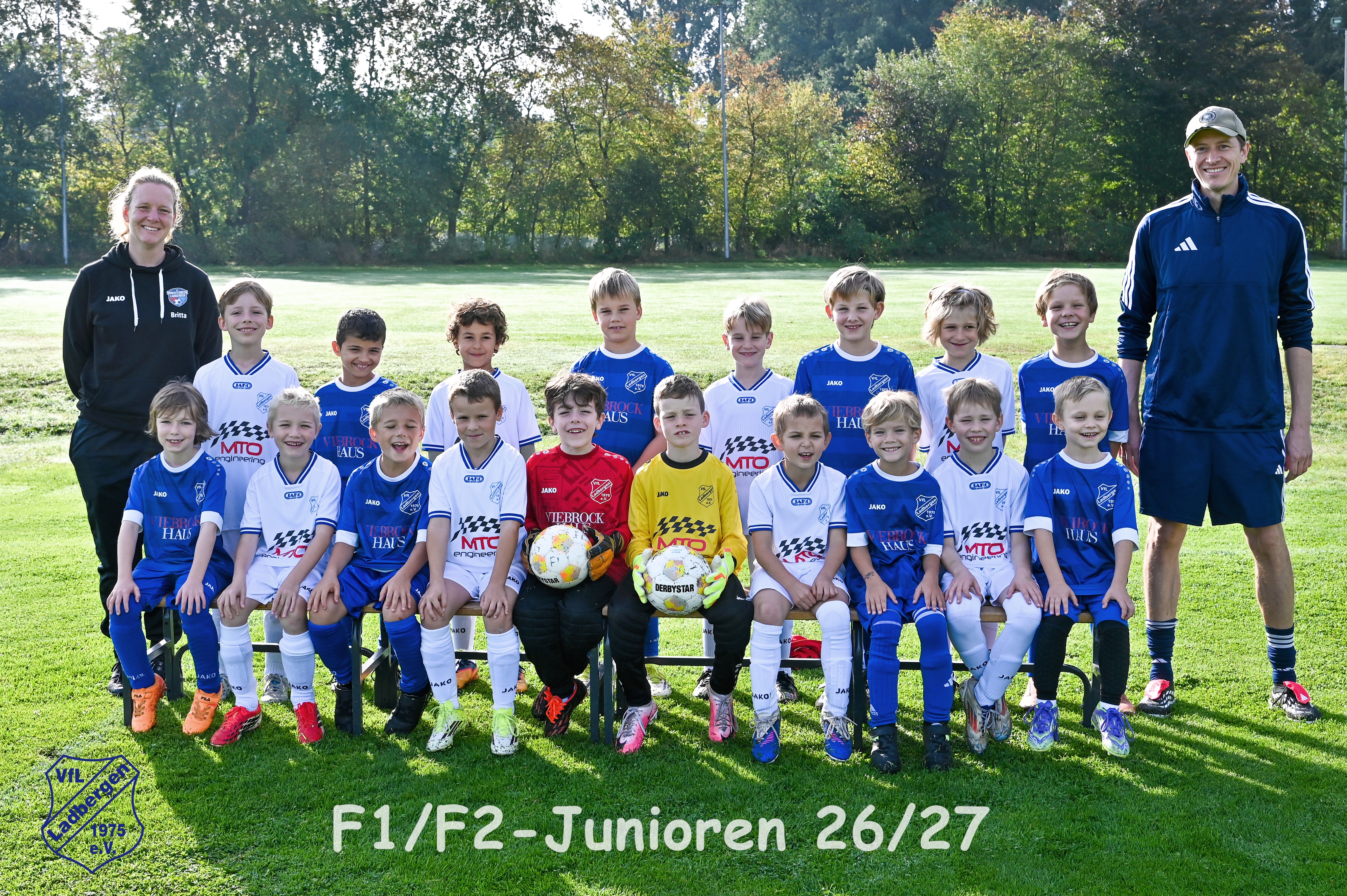 Laechelndes Kinderfussballteam mit zwei Trainern in blau weissen Trikots